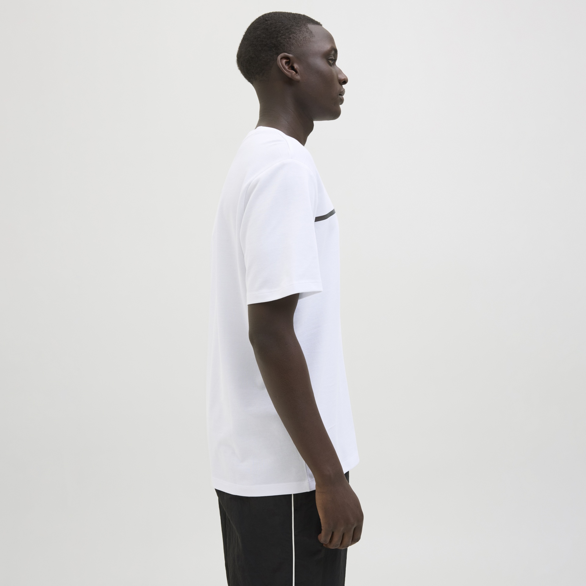 Homem de perfil com t-shirt branca e calças pretas com risca branca.