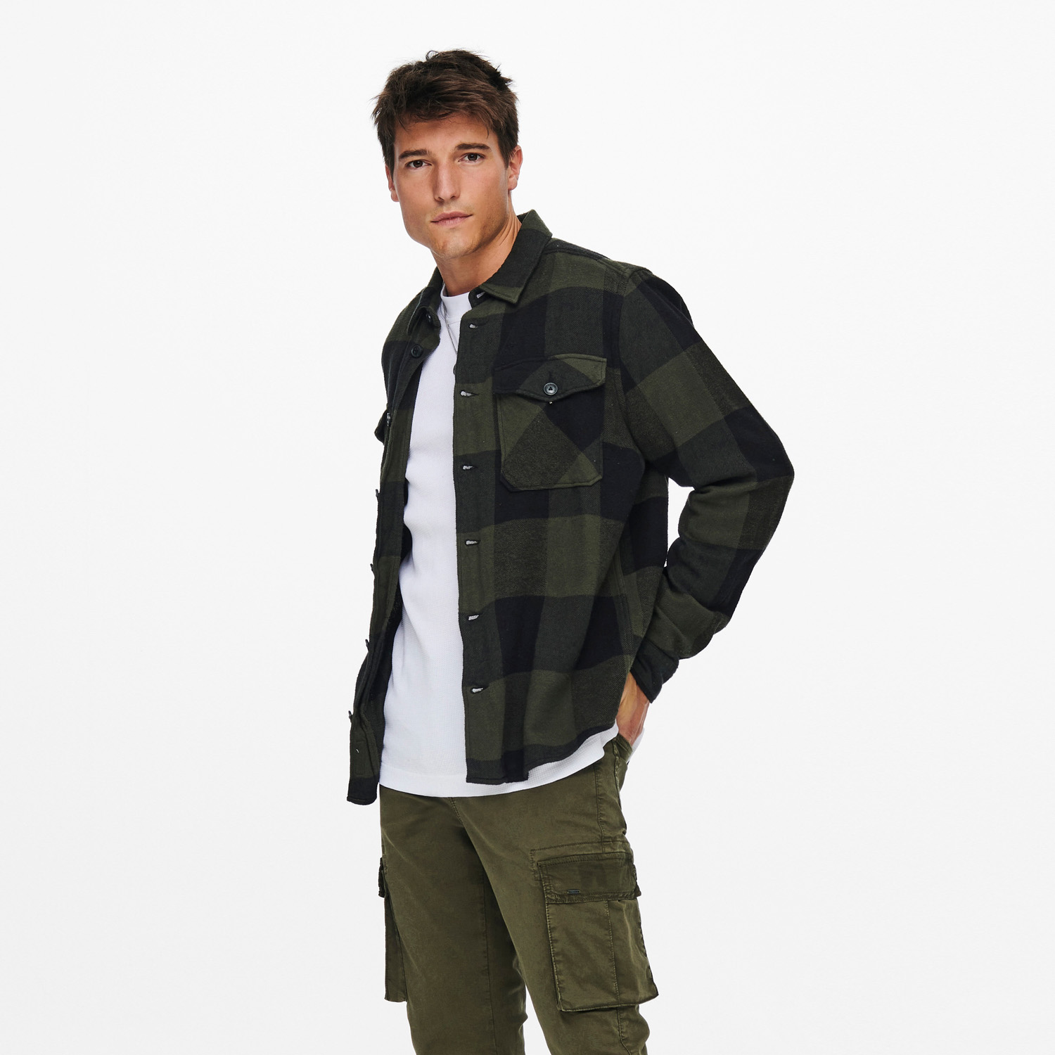 Homem com camisa xadrez verde e preta, t-shirt branca e calças cargo verdes.