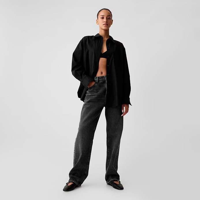 Mulher com camisa preta, jeans cinza escuro e sapatos pretos