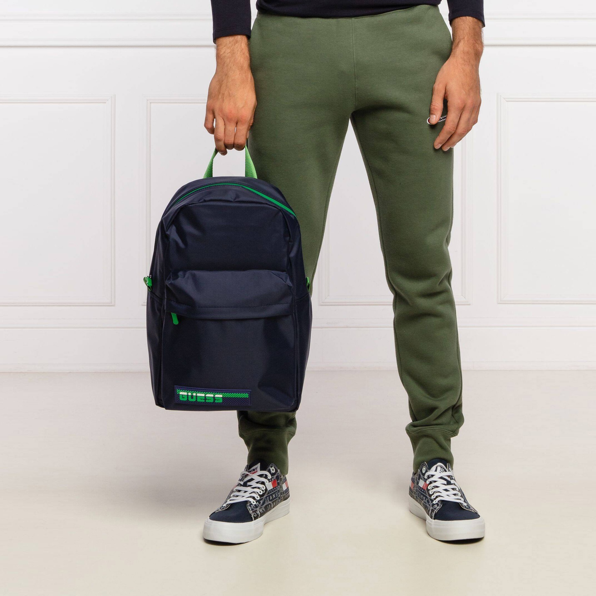 Mochila azul com detalhes verdes e bolso frontal com texto GUESS