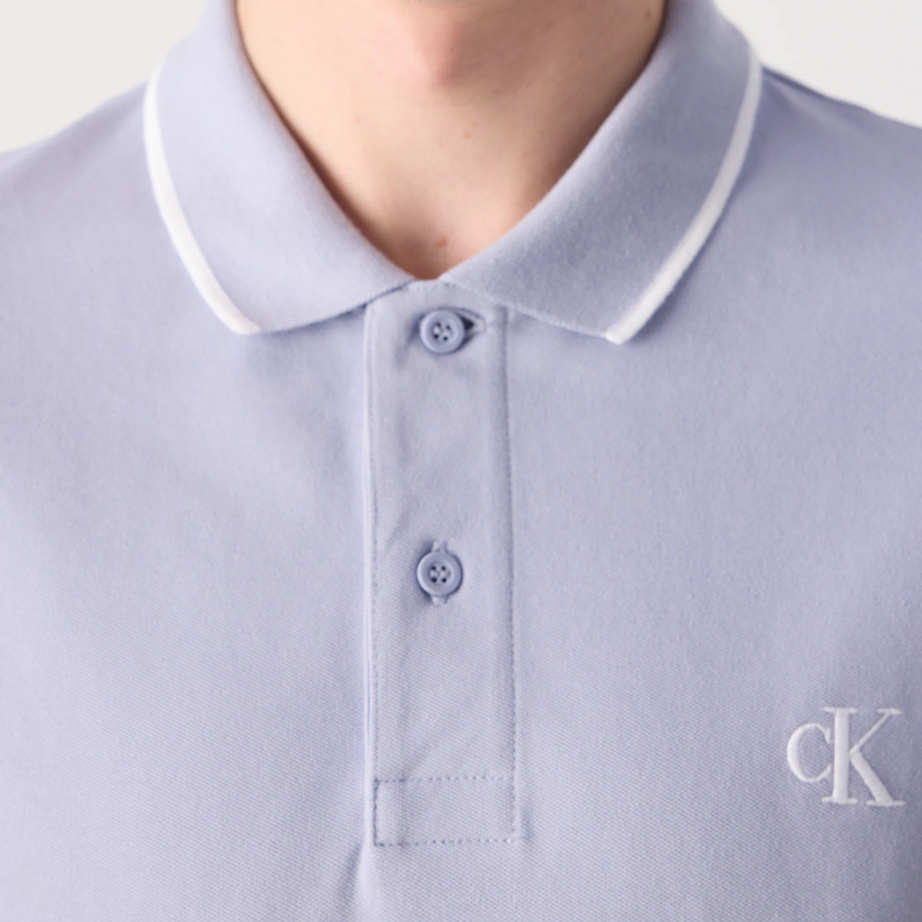 Polo azul claro com gola e borda branca, botões e logo cK bordado