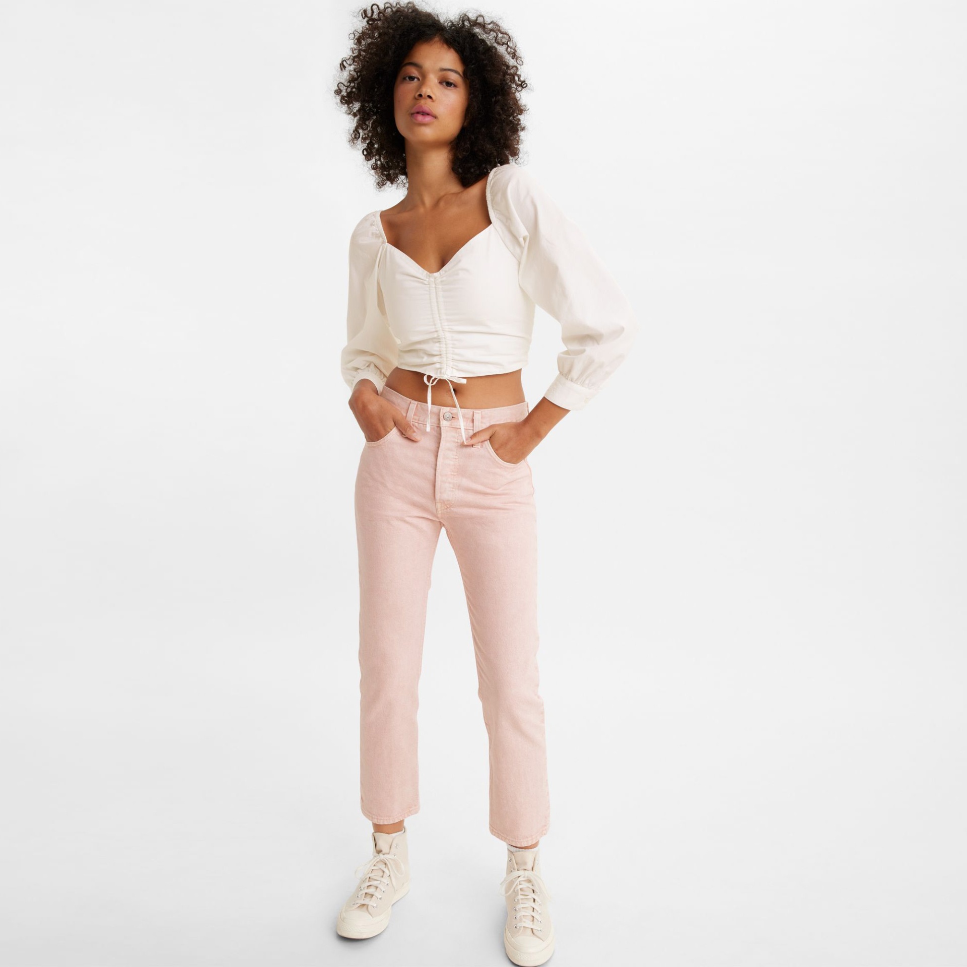 Mulher com blusa branca e calças rosa claras em fundo branco