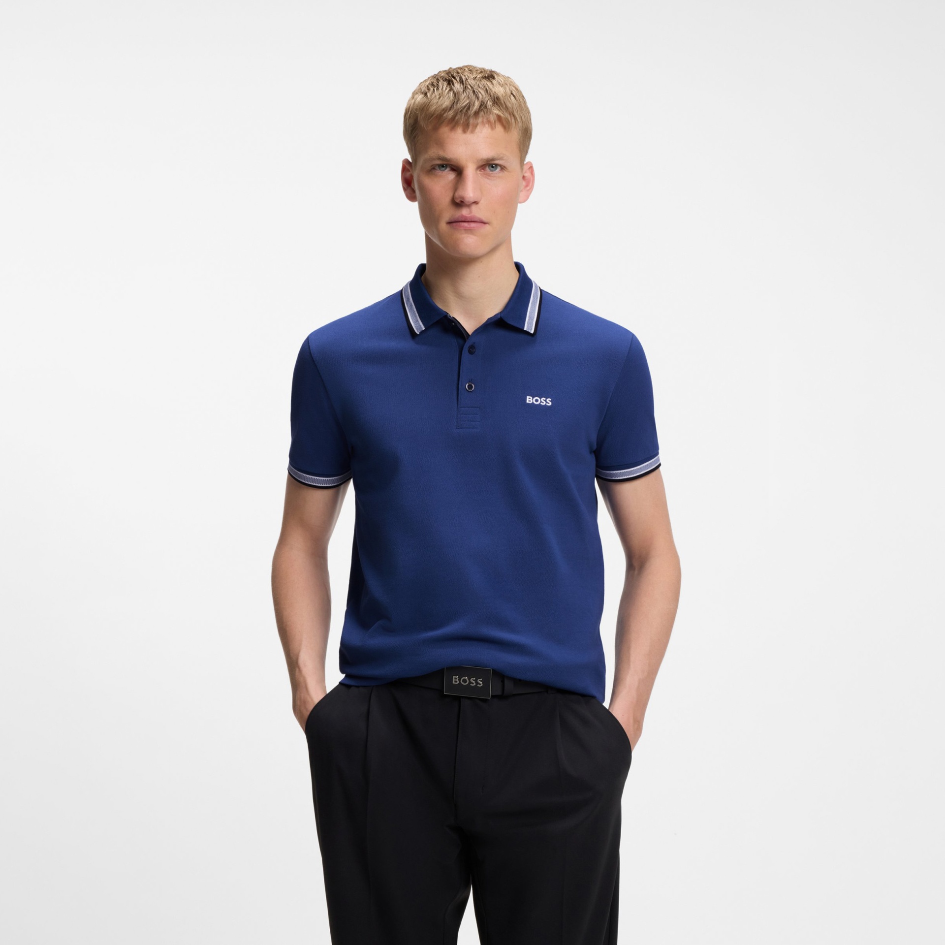 Homem com polo azul da marca BOSS com gola e punhos com listas brancas, calças e cinto pretos com logo BOSS visível.