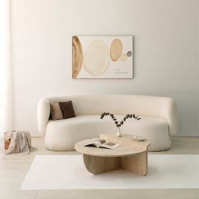Sala de estar com sofá branco curvo, mesa de madeira clara com vaso, almofadas castanhas e quadro abstrato na parede