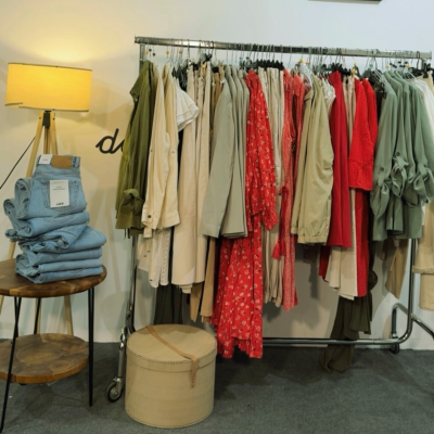 Várias roupas penduradas, jeans empilhados e candeeiro de pé em ambiente interno