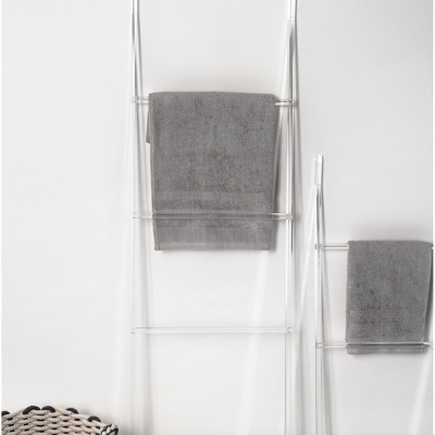 Toalheiros acrílicos transparentes com toalhas cinzentas penduradas numa parede branca e uma cesta trançada.
