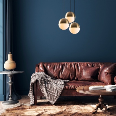 Sofá de couro castanho com manta cinza e candeeiros dourados suspensos numa sala de estar com parede azul.