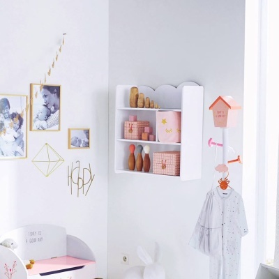 Quarto infantil decorado com prateleira branca, brinquedos de madeira, cabideiro e decoração de parede com molduras e texto.