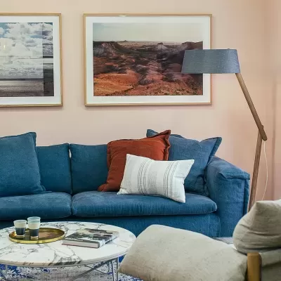 Sofá azul com almofadas, mesa de centro com tampo de mármore e candeeiro de pé de madeira e tecido azul