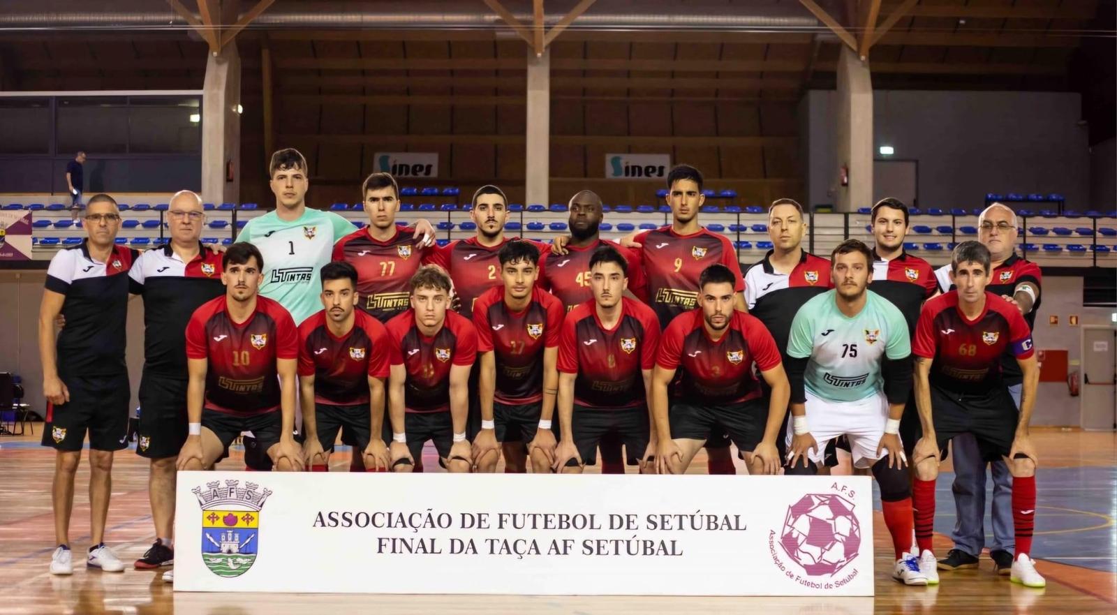 Equipa de futebol masculina posando em pavilhão com faixa da Associação de Futebol de Setúbal