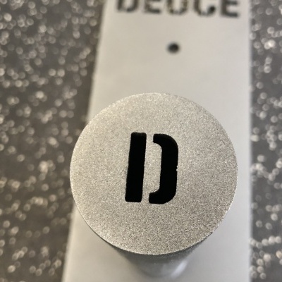 Tampa prateada com símbolo 'D' e texto 'DEUCE' ao fundo