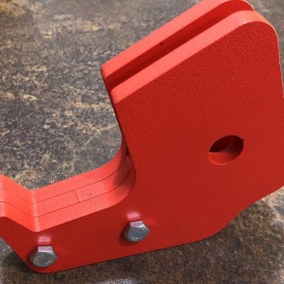 Peça metálica vermelha angular com parafusos sobre superfície escura rugosa