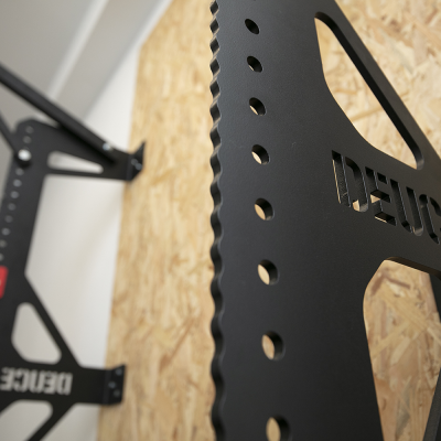 Estrutura preta metálica com texto recortado 'DEUCE' montada em parede de madeira