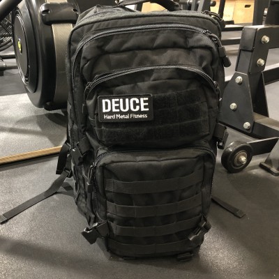 Mochila preta com etiqueta DEUCE Hard Metal Fitness no chão da sala de ginásio