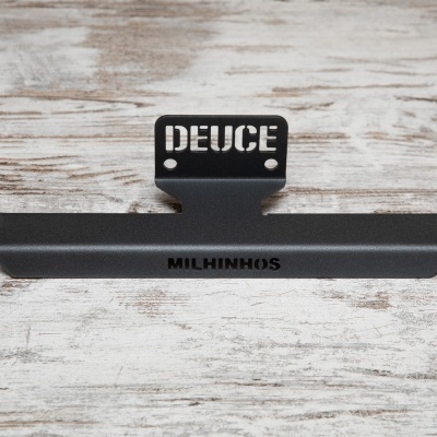 Suporte metálico preto com texto DEUCE e MILCHINHUS sobre madeira clara