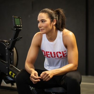 Mulher com colete branco e texto vermelho 'DEUCE' numa sala de ginásio escura
