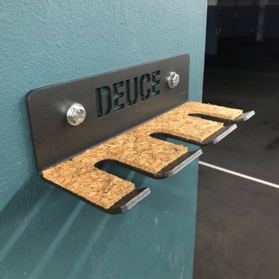 Suporte de parede metálico preto com cortiça para bicicletas, com recorte DEUCE, fixado na parede azul.