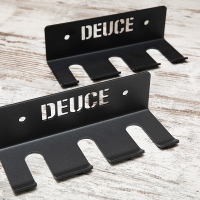 Suportes de parede de metal pretos com ganchos e texto DEUCE, sobre madeira clara.