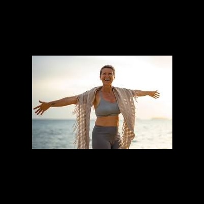 Mulher sorridente com roupa desportiva e xale bege junto ao mar