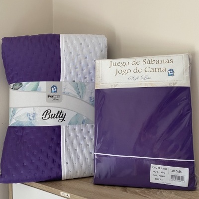 Conjunto de roupa de cama roxo e branco com padrão perfurado em embalagem na superfície de madeira.