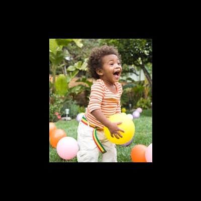 Criança a brincar com bola amarela num jardim verde com balões coloridos