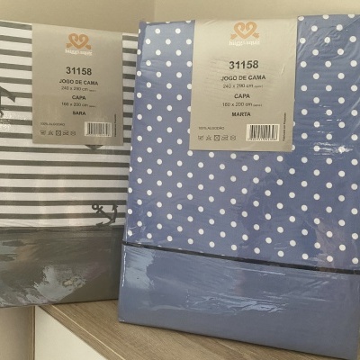 Dois pacotes de jogos de cama com padrão riscas cinza e bolinhas brancas sobre fundo azul