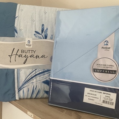 Roupa de cama azul e branca embalada com etiquetas visíveis numa superfície de madeira