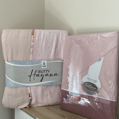 Conjunto de cama rosa claro embalado e outro com padrão floral em superfície de madeira