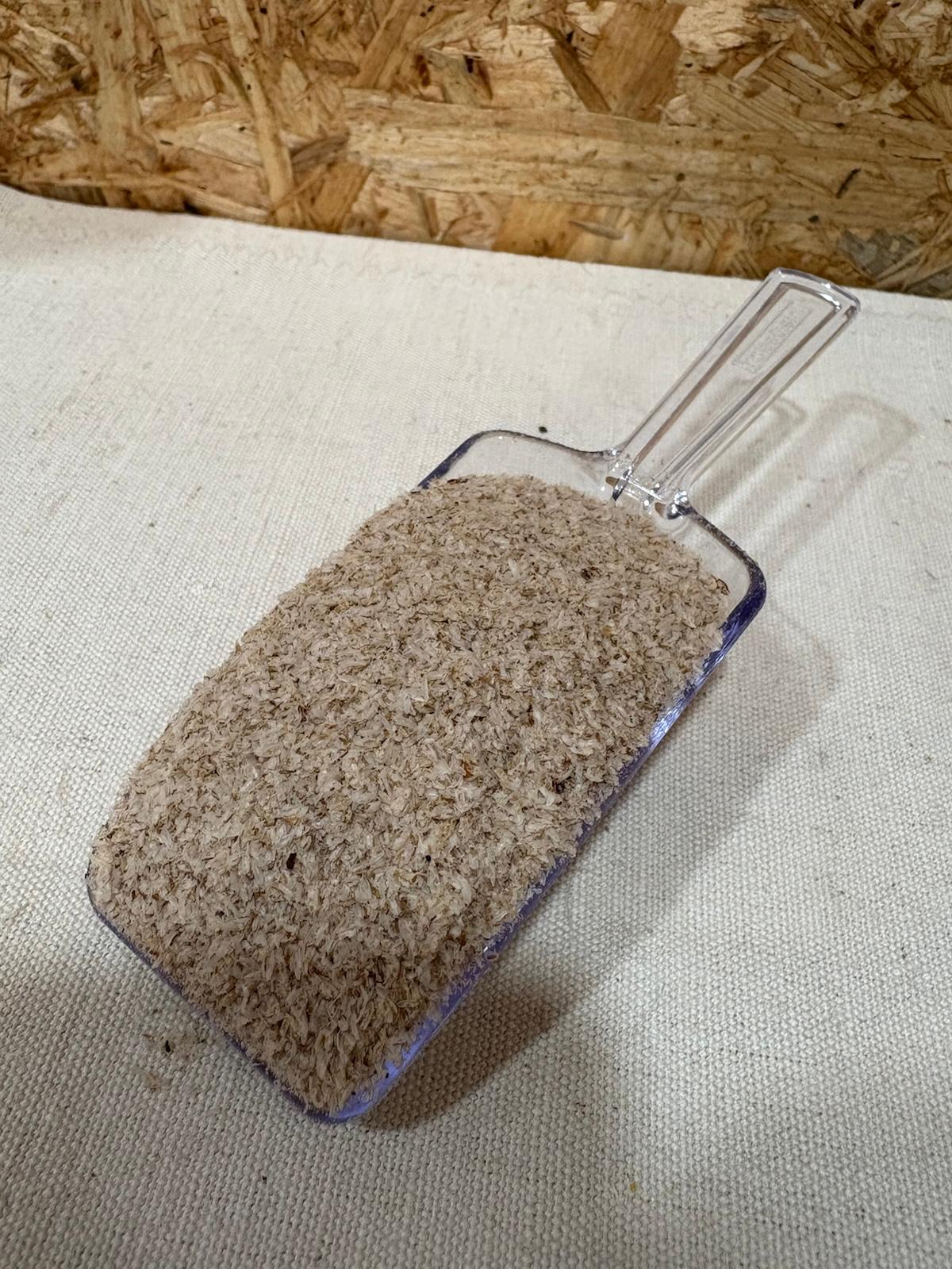 Psyllium Pá transparente cheia de pó marrom claro sobre tecido claro e fundo de madeira