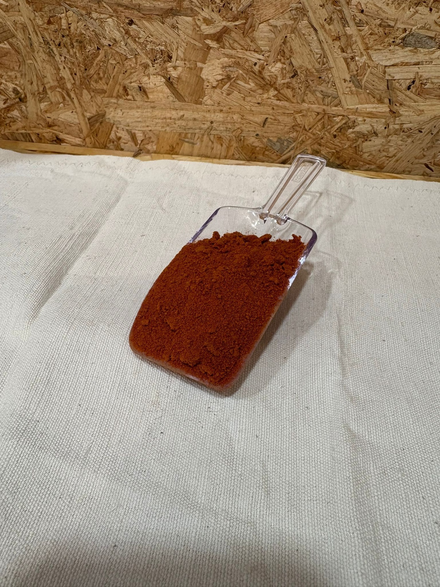 Farinha de Tomate Pá transparente com pó vermelho-alaranjado em tecido branco e fundo de madeira.
