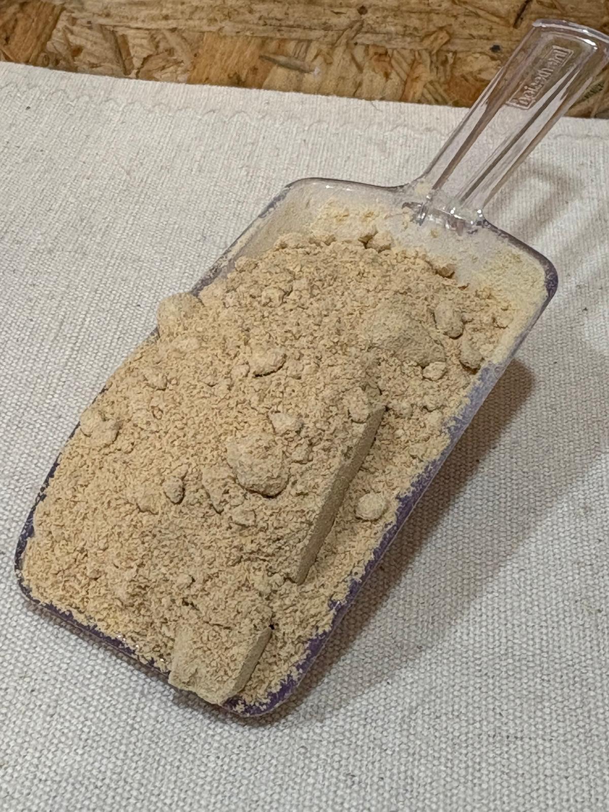 Maca em Pó Pá de plástico transparente com pó bege claro sobre tecido claro