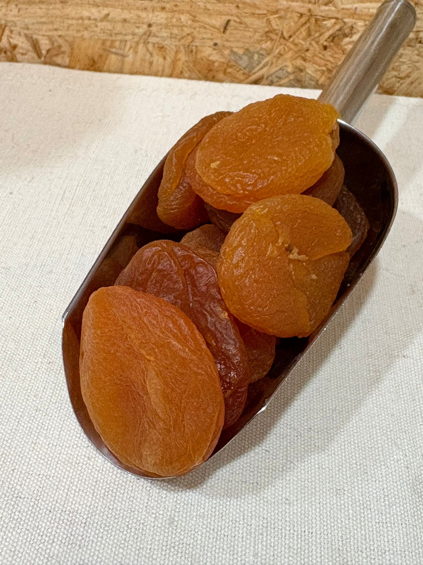 Alperce Seco Damasco seco laranja numa colher metálica sobre superfície branca com fundo de madeira clara