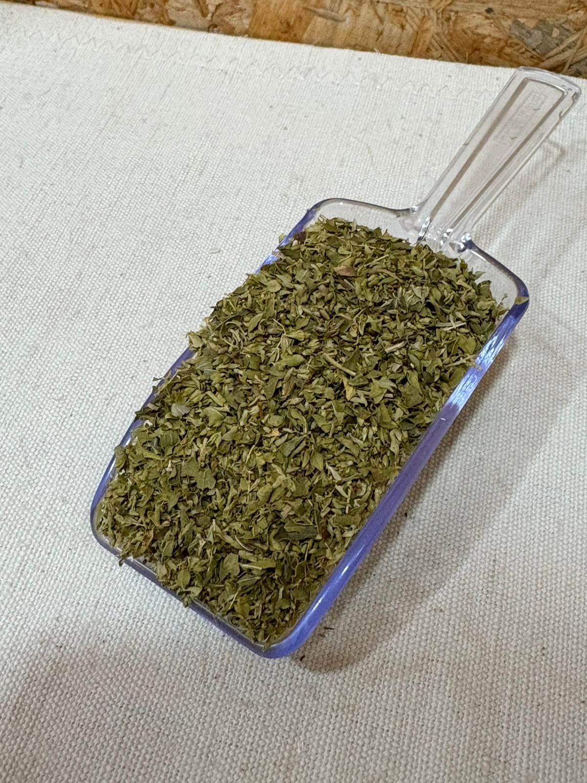 Oregãos BIO Pá plástica transparente com folhas secas verdes sobre tecido bege