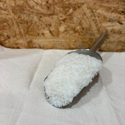 Colher metálica com flocos brancos sobre tecido branco com fundo de madeira OSB