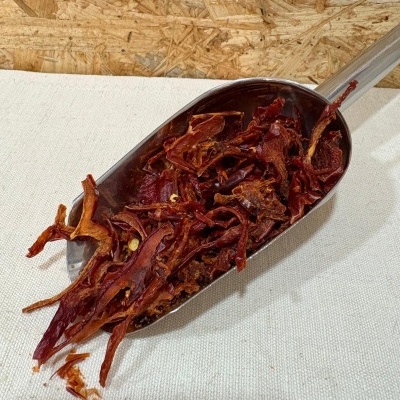 Colher metálica com pimentos vermelhos secos fragmentados sobre tecido branco