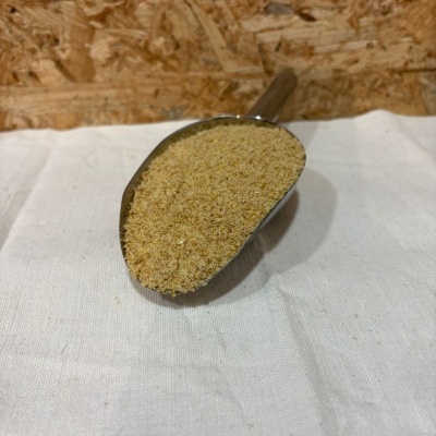 Colher metálica com pão ralado sobre tecido branco e fundo de madeira