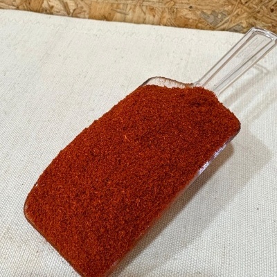 Colher de plástico com pó vermelho alaranjado sobre tecido branco e fundo de madeira