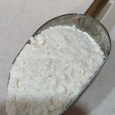 Pá metálica com cabo de madeira cheia de pó branco sobre tecido branco