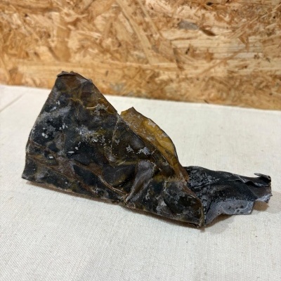 Pedaço de alga marinha seca castanha escura com textura enrugada sobre tecido claro com fundo de madeira