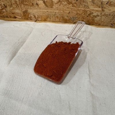 Pá transparente com pó vermelho-alaranjado em tecido branco e fundo de madeira.