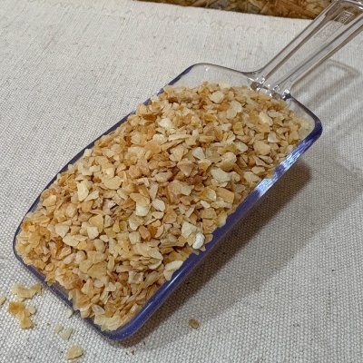 Pá plástica com flocos dourados secos sobre tecido bege e fundo de madeira