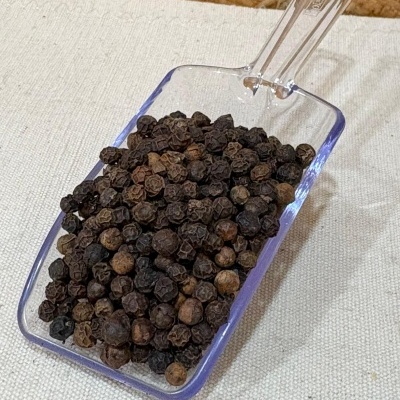 Pimenta preta em grão numa pá transparente sobre tecido bege