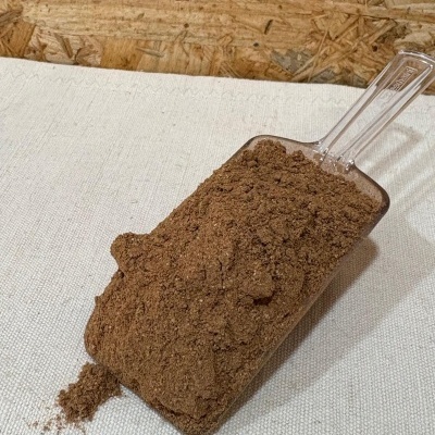 Pá plástica com pó castanho sobre superfície têxtil branca e fundo de madeira