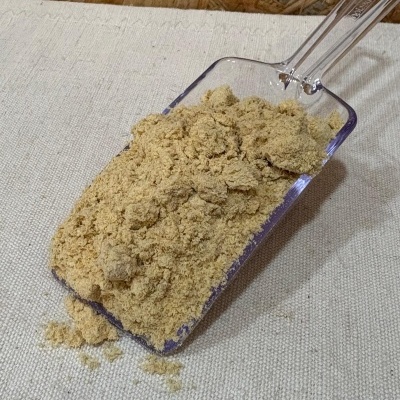 Pá transparente com pó castanho claro sobre tecido bege e fundo de madeira.