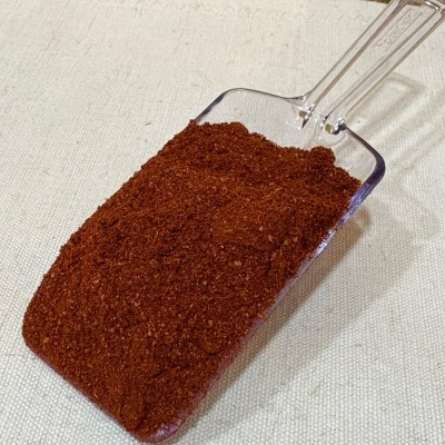 Espátula transparente com pó vermelho escuro em superfície clara e fundo de madeira