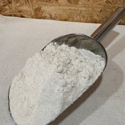 Colher metálica cheia de farinha branca sobre tecido bege com fundo de madeira OSB