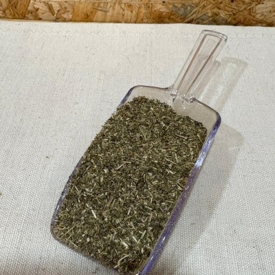 Pá de plástico com ervas secas verdes e castanhas sobre tecido bege e madeira aglomerada