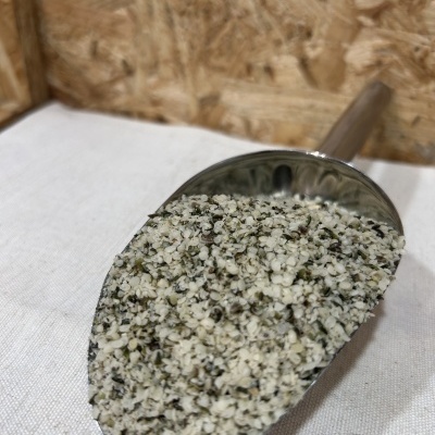 Colher metálica com sementes de cânhamo sobre tecido branco e fundo em madeira aglomerada