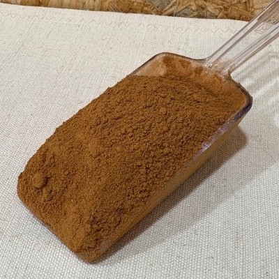 Colher de plástico com pó castanho sobre tecido branco.