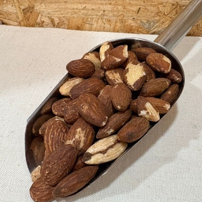 Concha metálica com amêndoas com casca sobre tecido branco e fundo de madeira OSB